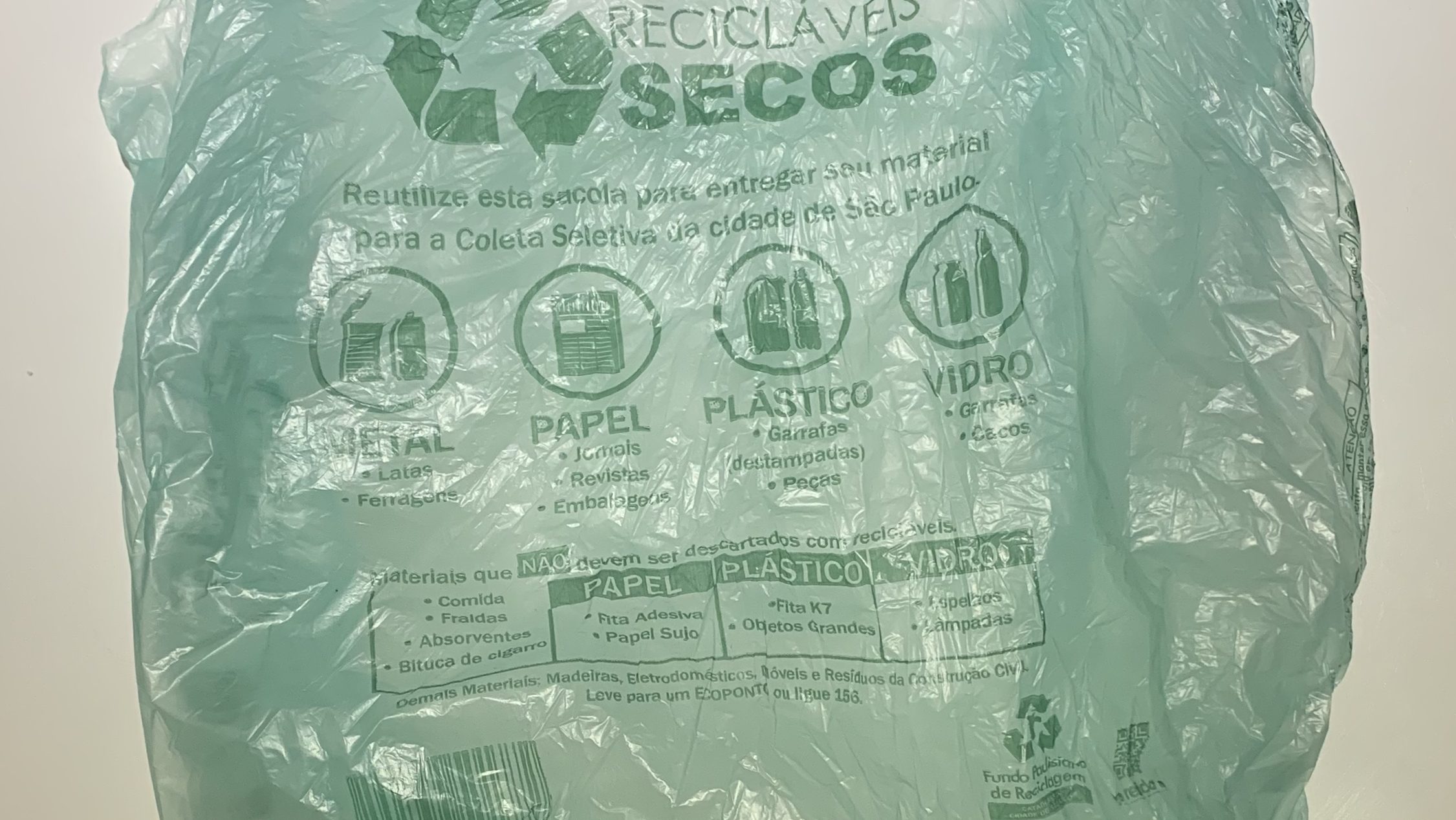 A green plastic grocery bag. It has various text related to recycling procedures. 