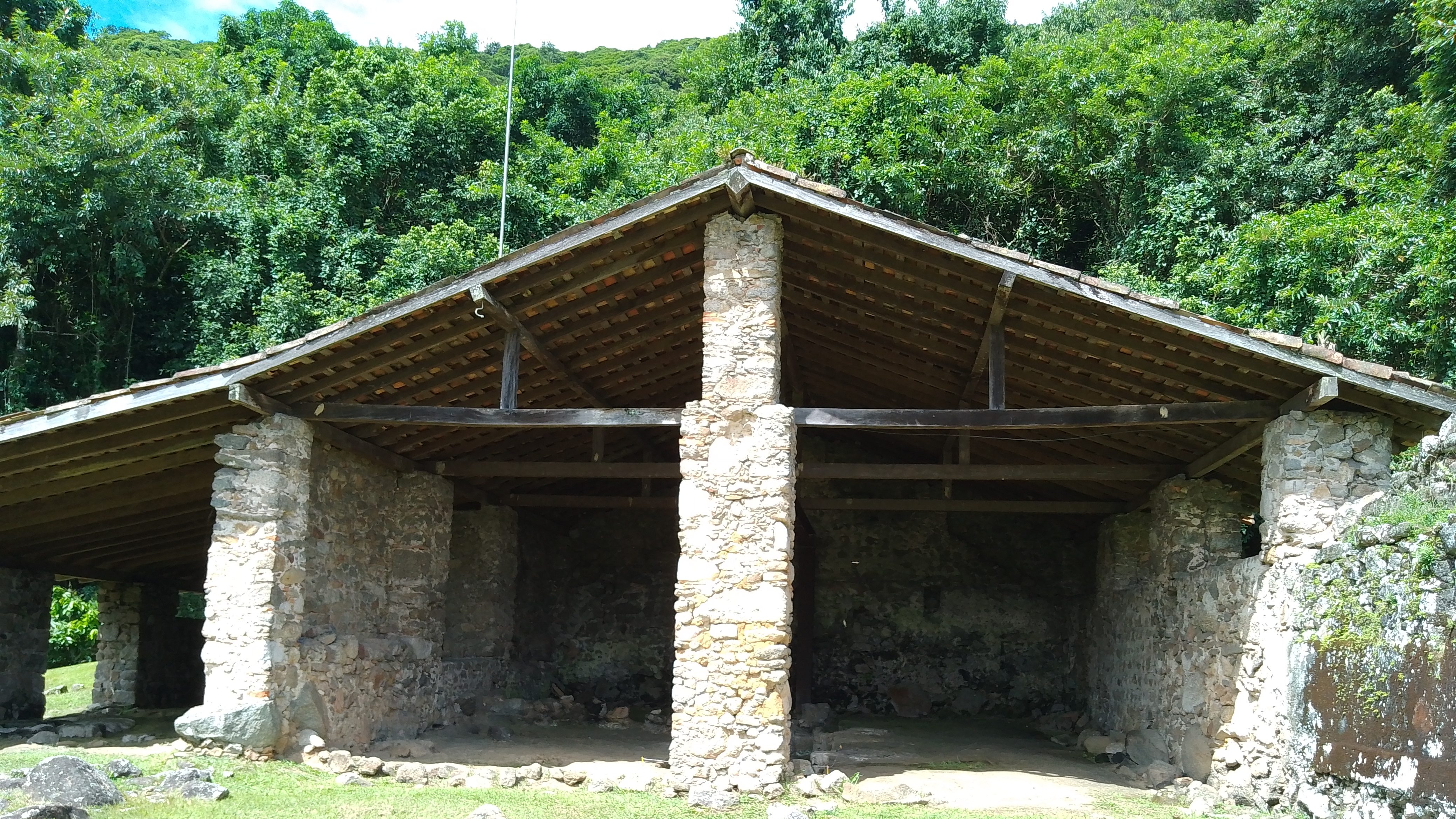 The ruins of an old stone structure stand in front of a dense tropical forest. 